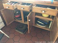 Open kitchen cabinets showing various pots, pans, casseroles including Dansk enamel dishes and colanders.