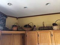 Overhead view of top of wooden cabinets showing several woven baskets, a bean pot, and a figurine on top