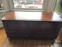 Full front view of large wooden hope chest showing flat top, paneled doors, and bottom drawer with handles.