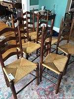 Six wooden ladderback chairs with woven rush seats arranged in a group on a patterned rug.