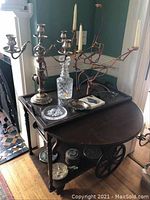 Overview of two silver-plate candelabras, glass decanter, metal dish, and glass plate on dark wood table.