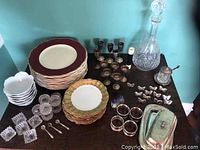 Overview of lot showing plates, bowls, glass salt cellars with spoons, metal goblets, napkin rings, butter dish, crystal decanter, and more