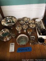 Group shot of all sterling silver items on wood floor: large bowl, pedestal cups, plates, spoons in box