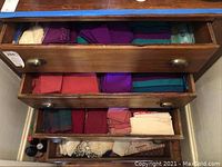 Four wooden drawers filled with stacked cloths and napkins in varied colors and folded neatly.