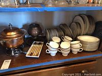Copper chafing dish on metal stand, copper fondue pot, wooden-handled forks, Palatia china cups and plates on shelf