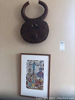 Full view of the mask mounted above the framed abstract drawing on a wall.
