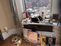 Overall view of art supplies including easel, paintbrushes in container, paper pads, paint tubes in bags and palettes on window ledge.