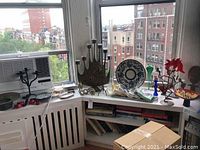 Large metal candelabrum with seven candle holders, ceramic plates, colorful cocktail napkins, and decorative items shown on window ledge under natural light.