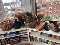 Overview of several woven baskets, copper-finish pitcher, metal planters, wood figurine, and other small decor items on a white bookshelf by window