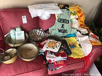 Overview of nested ceramic bowls, various kitchen textiles including aprons, dish towels, pot holders, and two small green and white cans.