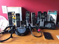 Multiple cordless phone handsets from AT&T and Panasonic, an Insignia compact disc player, wired headphones, and a black Apple iPod on a table.