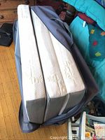 Three-piece folding mattress inside a zippered carrying case, showing the thickness and closure.