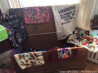 Photo showing a wooden chest open with an assortment of colorful woven fabrics, scarves, pillowcases, laundry bag, and small items inside.