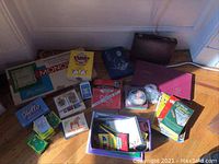 Full assortment of games and art supplies grouped on a wooden floor showing multiple items including Monopoly box, card games, and art supplies.