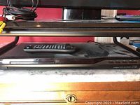 Front view of black Insignia DVD player with remote on top, cables visible on side, placed on marble surface.