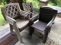 Four black metal frame patio chairs with cloth seats and backs next to some plastic chairs, all outdoors on a patio.