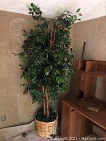 Full view of tall faux tree with woven basket pot against wall.