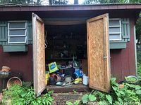 Wide shot of open shed with visible garden supplies, planters, hose, and chairs inside and outside.