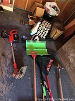 Black & Decker cordless trimmer and assorted yard tools including shovels, rakes, hoe