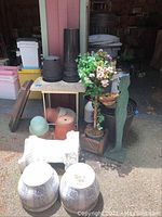 Full view of various planters including plastic, terracotta, ceramic, a tall black plastic planter, white plaster pedestal with broken top, and cement table.