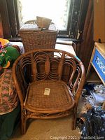 Rattan style chair with woven seat, visible curves of armrest and back supports, placed near window.