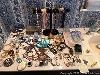 Overview of assorted jewelry on bathroom countertop including watches, necklaces, bracelets, earrings, charms