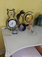 Photo of tabletop with two clocks, black carved palm tree figurine, light beige carved stone figurine, clear glass dish, and small digital timer.