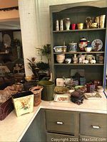 Wide view of pottery and planters on shelves and countertop including cement planters, ceramic canisters, and decorative items