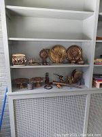 Shelf holding various metal plates, animal figurines, horseshoes, candlestick, and decorative horn