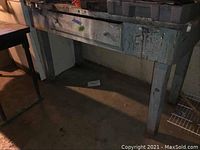 Full view of the wood workbench showing the single drawer and the painted splatters on drawer and legs.