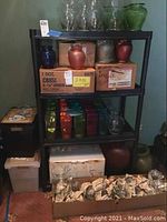 Black shelving unit with colorful and clear glass vases on shelves, boxes underneath and votive candle holders in box in front