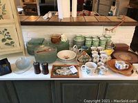 Table full of various kitchenware items including glass plates, cups and saucers, bowls, wooden trays, and miscellaneous items