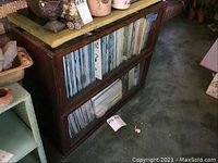 Front view of wood framed two-section barrister bookcase with glass fronts, filled with magazines or books inside.
