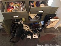 Contents of a green wooden cabinet including office supplies, vintage phones, cables, tape dispenser and folders on the floor and in drawers.