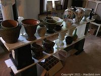 Wide view of the collection displayed on a white shelf supported by black stands showing a variety of planters, vases, and storage containers.