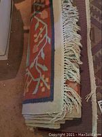 Folded floral patterned area rug showing fringed edges and folded layers.