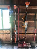 Three handheld tools hanging on wall, two red gas cans and scattered accessories on floor