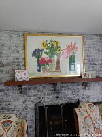 Framed print displayed on brick fireplace mantel with chair arms visible