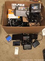 View of all Garmin and Navigon GPS devices placed on floor with bundled cables and mounts inside a cardboard box