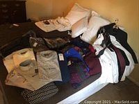 Overall view of three black tuxedo jackets on hangers, folded sweaters and dress shirts on bed