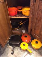 Cupboard shelf showing top two enameled cast iron Dutch ovens and two non-stick skillets on middle shelf