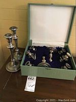 Two assembled tall candlesticks alongside green box containing silver components