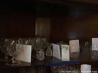 Shelf view showing nine footed goblets at left, small lidded jar, small pitcher and six tumblers at right.