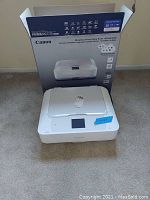 Printer placed on carpet floor with box behind it showing model and features