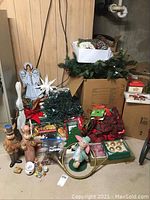 Overview of assorted holiday decorations including wooden bunnies, angel, wreaths, ribbons, lights, and small figurines on concrete floor