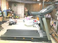Side and top view of NordicTrack C700 treadmill in a cluttered basement environment showing the running deck and part of the control console.
