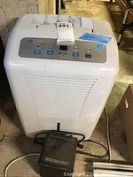 General Electric white dehumidifier with control buttons and indicator lights on top panel, cord visible, placed on concrete floor.