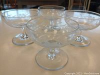 Four clear crystal dessert glasses shown grouped on a table, side view, highlighting the etched floral designs around the bowls.