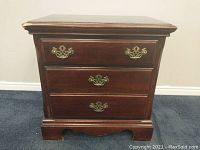 Front view showing the brown wooden end table with three drawers and decorative brass handles.