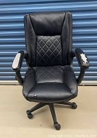 Front view of the black leatherette massage office chair showing diamond quilted upholstery, peeling on armrests, and wear on seat.